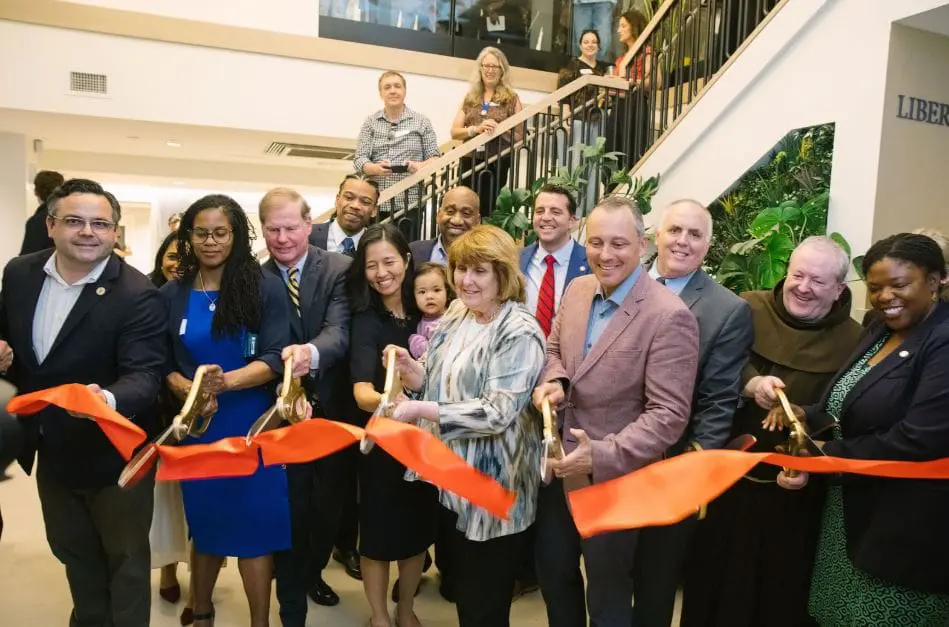 Diverse group of professionals cutting a red ribbon at a ribbon-cutting ceremony in a lobby or atrium.
