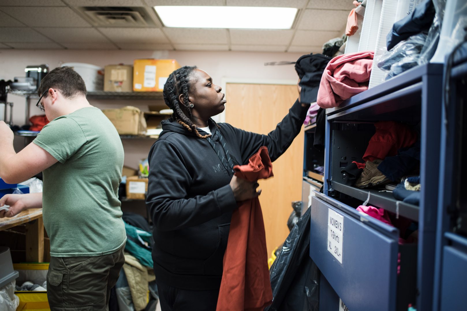 An employee and a volunteer sort and organize clothing in a storage room.