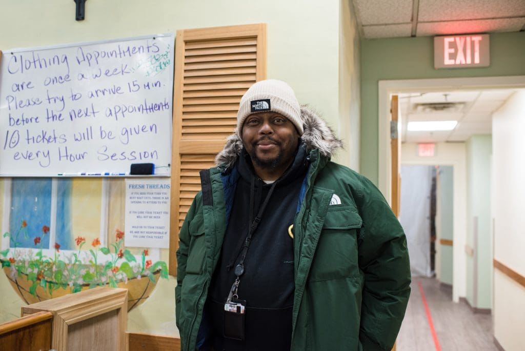 SFH Guest - St. Francis House A guest dressed in winter clothing stands in our clothing center, smiling.